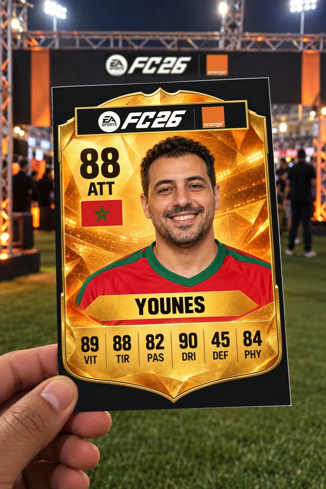 Une main tient une carte de joueur aux logos EA SPORTS FC 26 et Orange, avec le portrait souriant d’un supporter, Younes, note 88, devant le stand