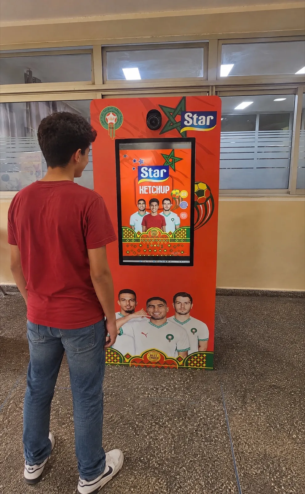 Un adolescent se place face à la borne photo rouge Star, qui l’affiche déjà au centre de l’étiquette, entre les joueurs
