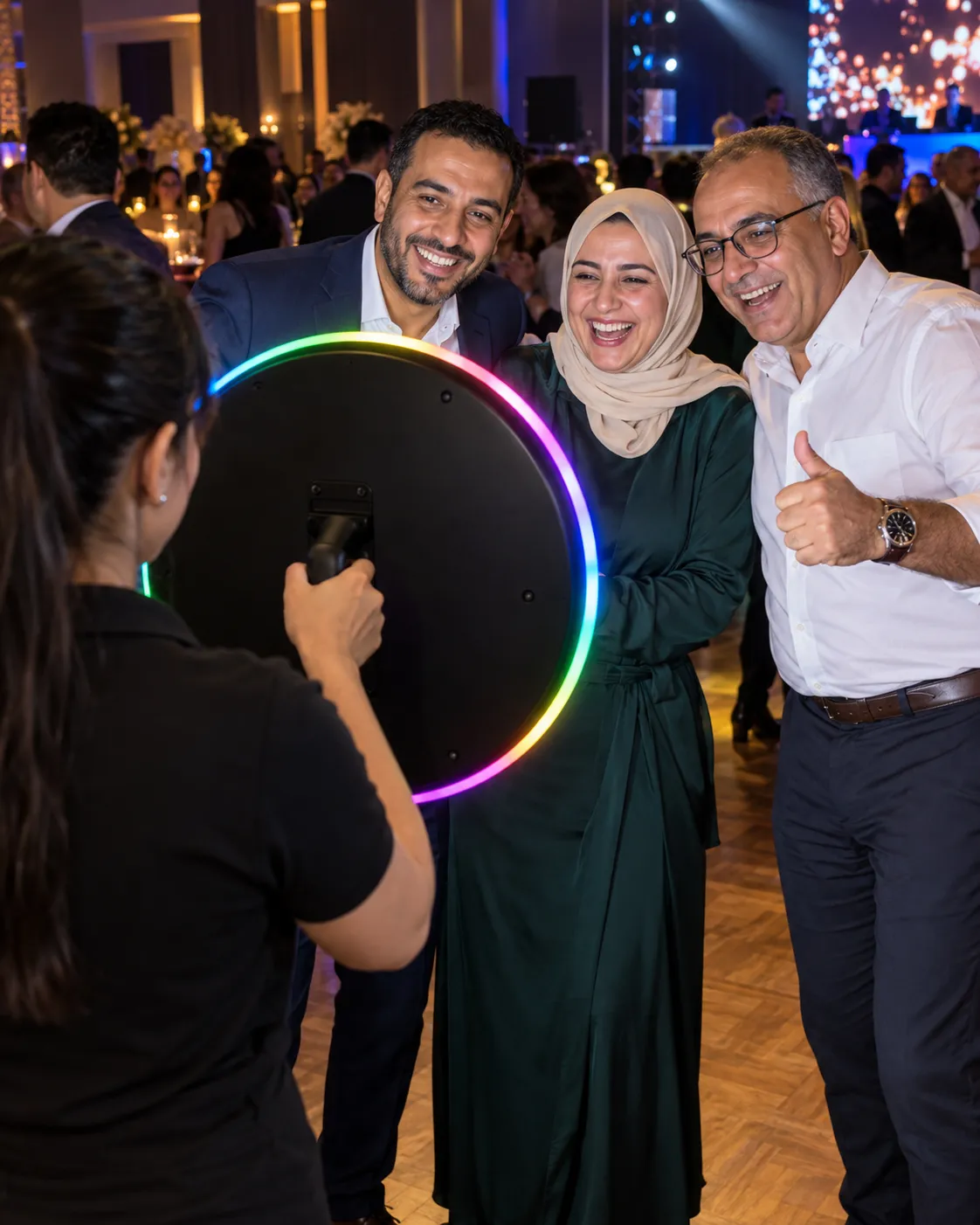 Soirée d’entreprise : trois collègues posent face à l’anneau lumineux multicolore, vu par-dessus l’épaule de l’animatrice