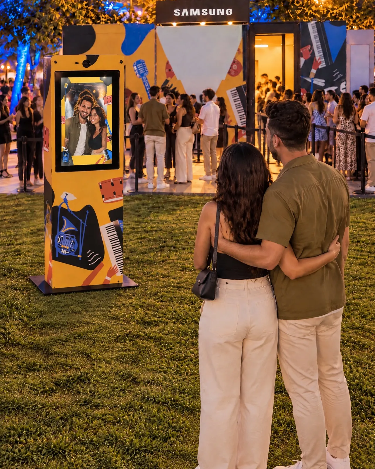 Devant le stand Samsung, un couple prend la pose face à la borne photo IA, dont l’écran portrait affiche leur pochette