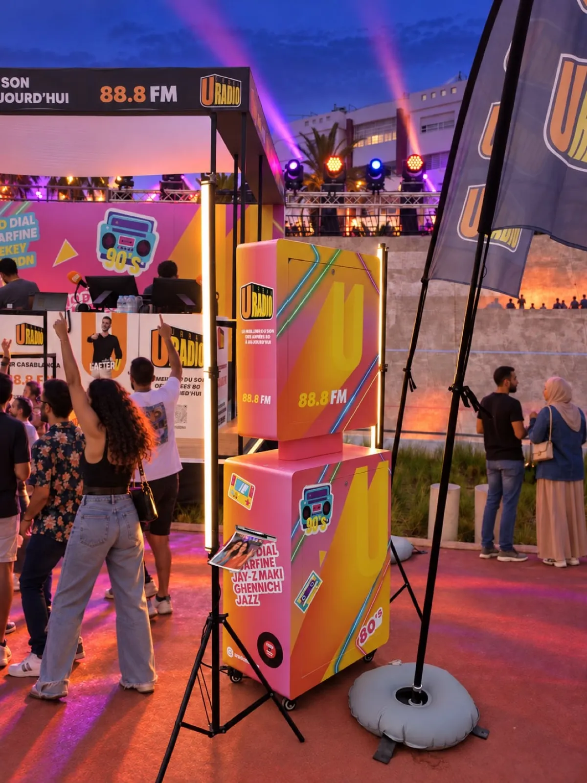 La Selfie Box U Radio vue de côté, devant la scène éclairée et le studio de la radio, pendant que des festivaliers dansent sur la piste du vélodrome