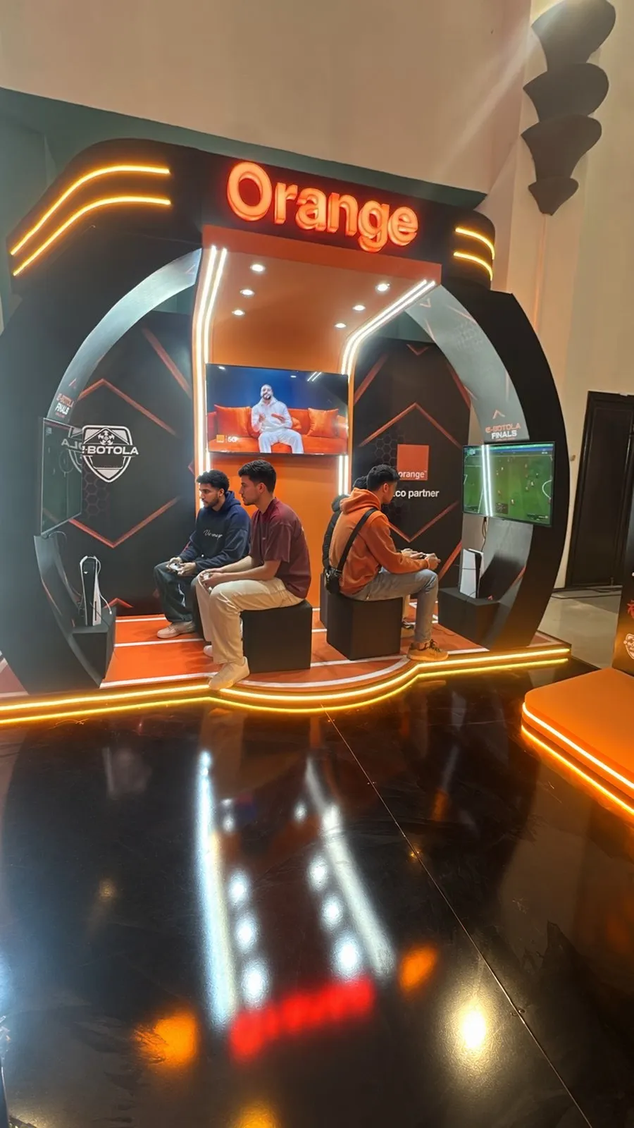 Des jeunes joueurs, manette en main, s’affrontent sur EA SPORTS FC 26 sous l’arche lumineuse du stand Orange