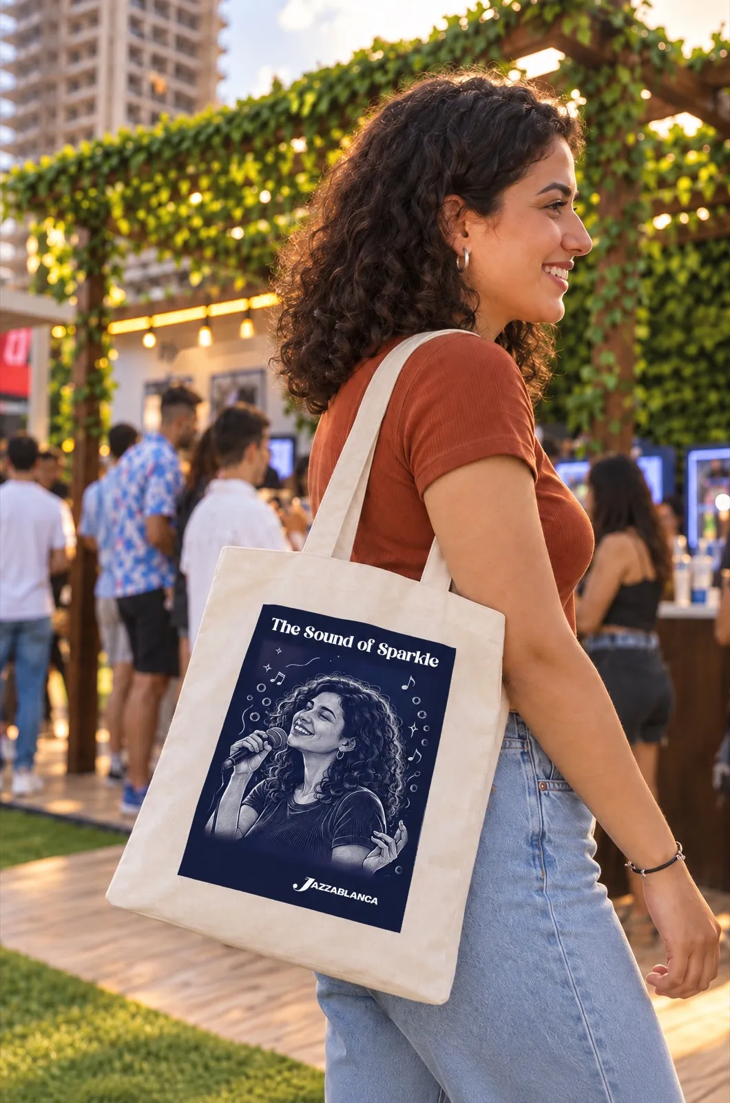 Un tote bag The Sound of Sparkle porté à l’épaule, festival en arrière-plan